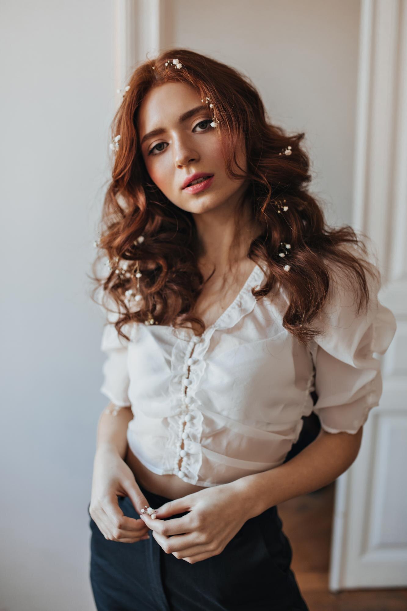 Portrait young girl with red wavy hair dressed black pants white blouse romantic woman with flowers her hair posing white room 197531 26445